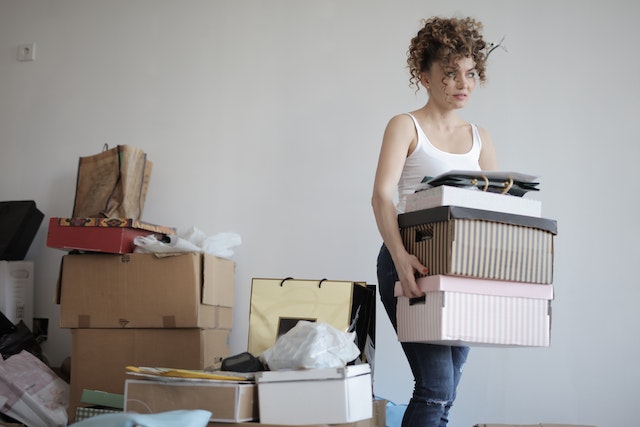 Young woman carrying a stack of cardboard boxes to a storage unit, representing one of the tips for dealing with sentimental clutter.