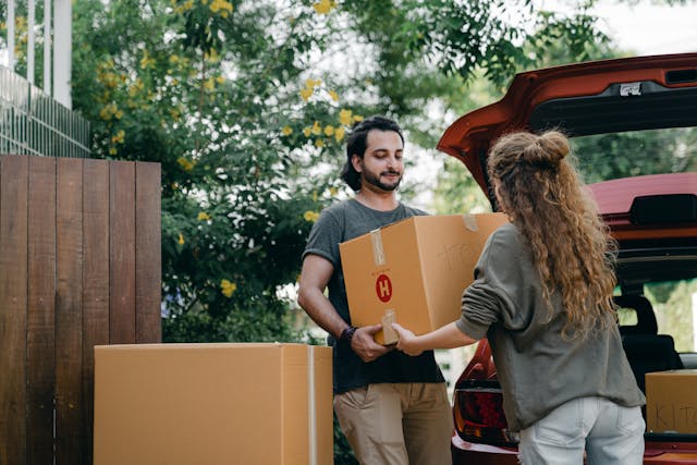 A couple moving boxes into a car, preparing for a move while navigating state regulations for a smooth relocation